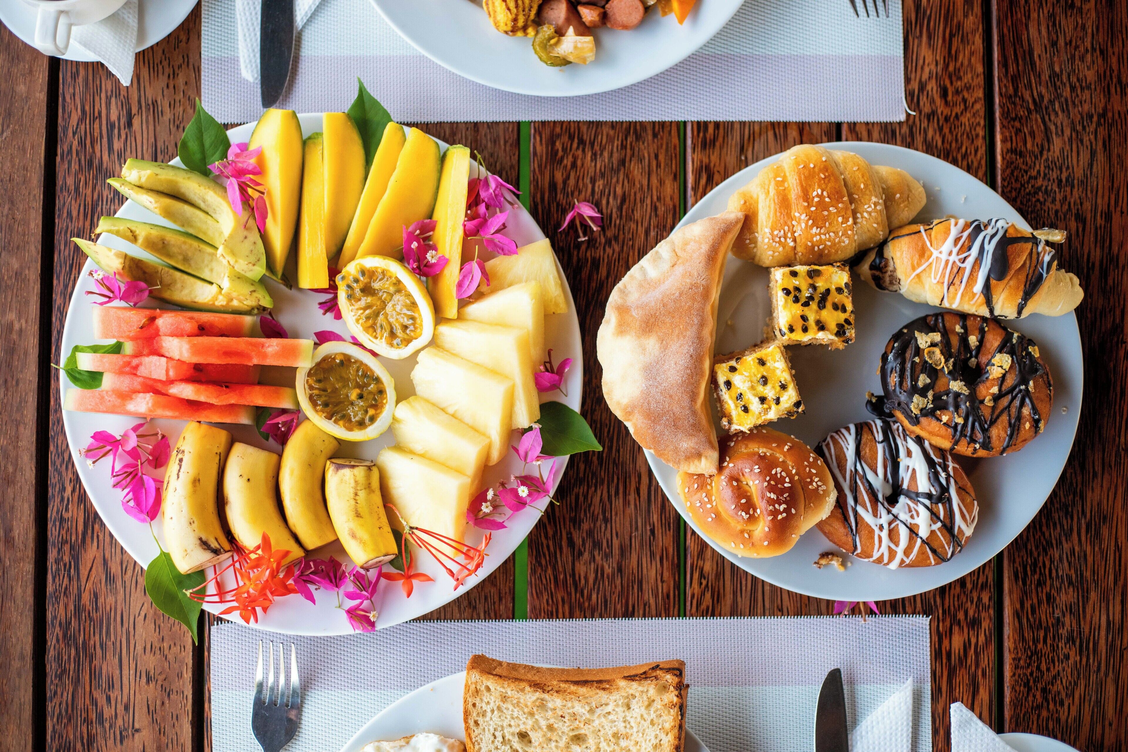 Una mesa de madera con dos platos de comida, uno con frutas y verduras en rodajas, y el otro con pasteles y pan.