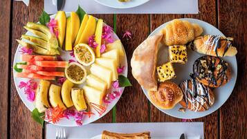 Una mesa de madera con dos platos de comida, uno con frutas y verduras en rodajas, y el otro con pasteles y pan.