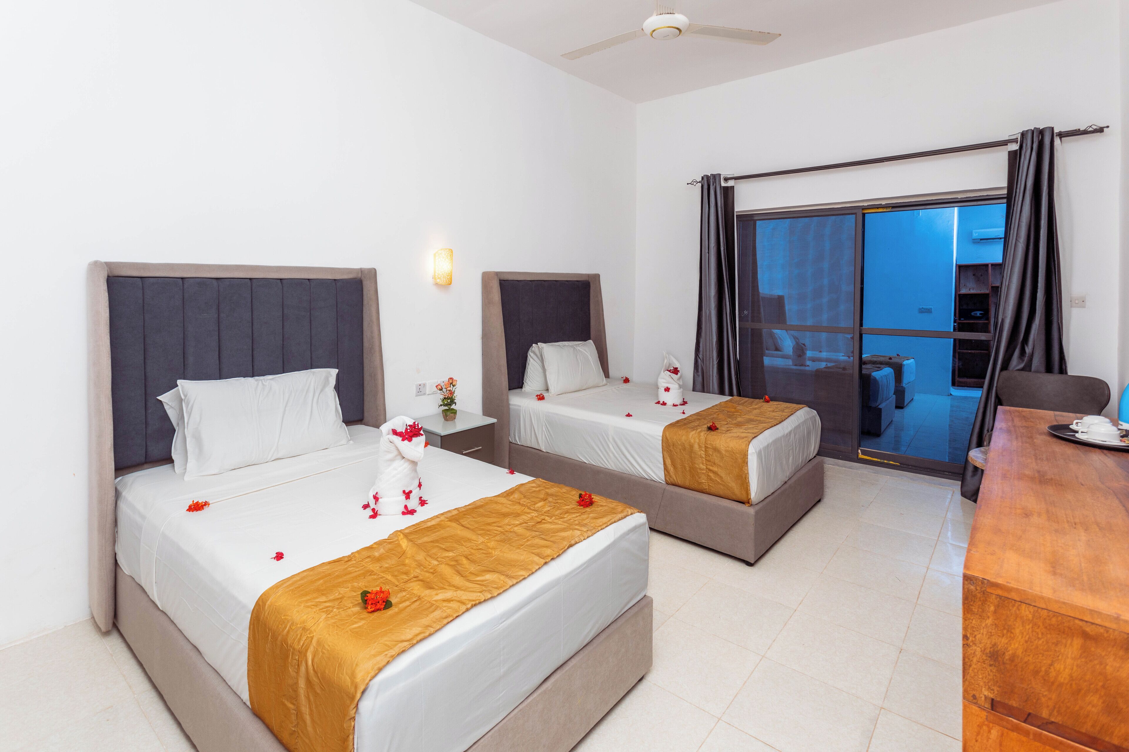A hotel room with two beds, a desk, and a view of the outside.