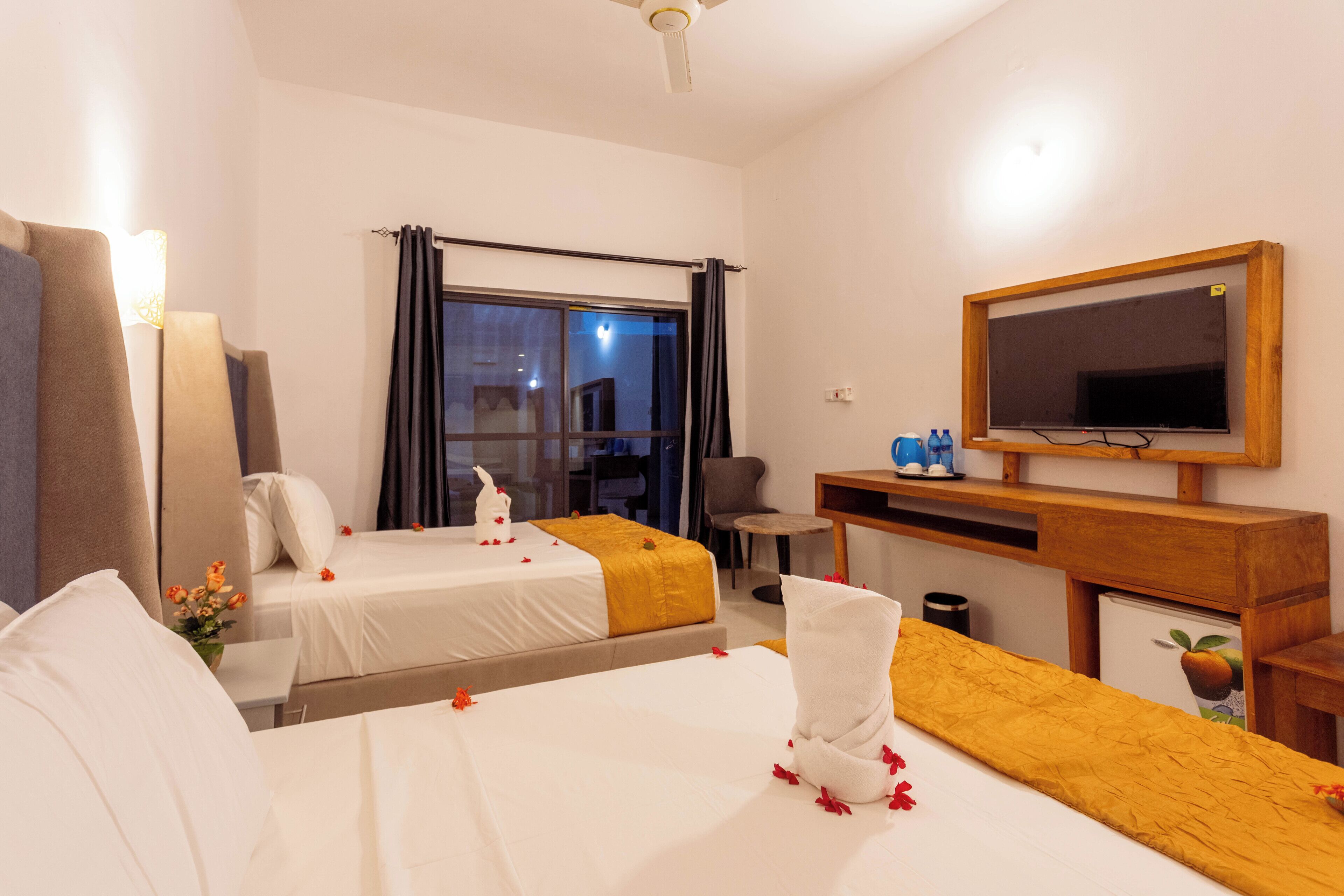 A hotel room with two beds, a TV, a desk, and a window with curtains.