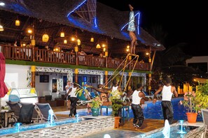 Zona de piscina con sillones de descanso, un bar y una estructura con techo de paja.