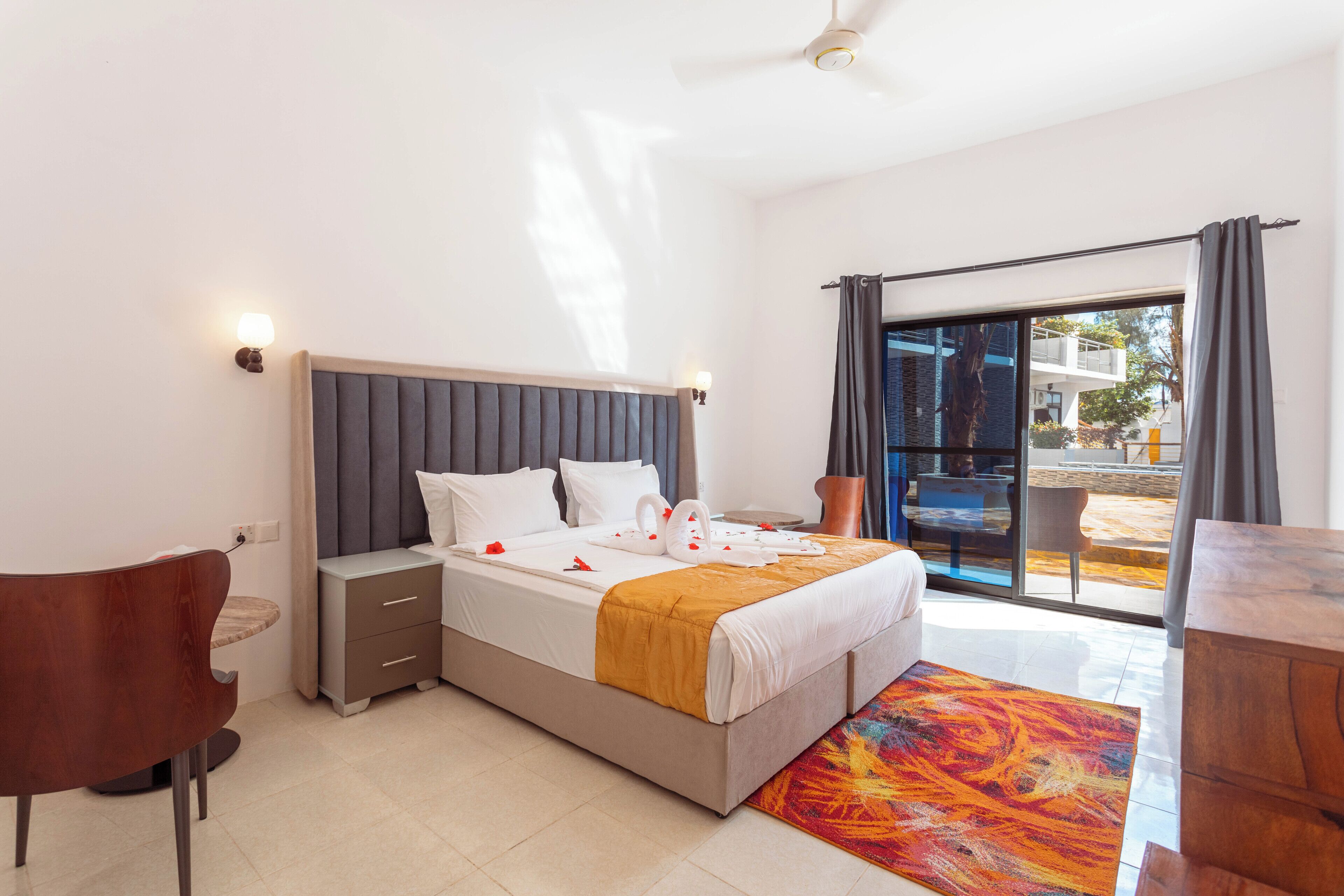 A modern hotel room with a bed, bedside table, chair, and a view of the outside.