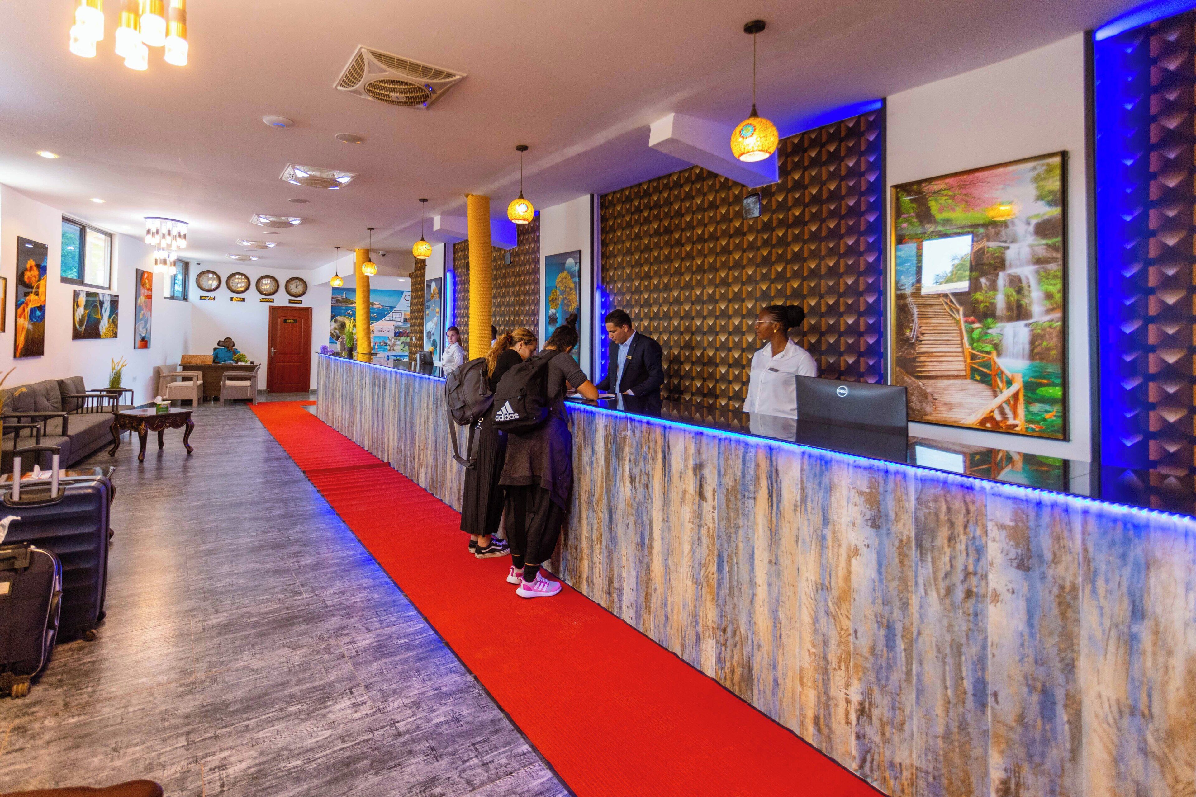 A hotel reception area with a red carpet, a reception desk, and a wall with a textured pattern.