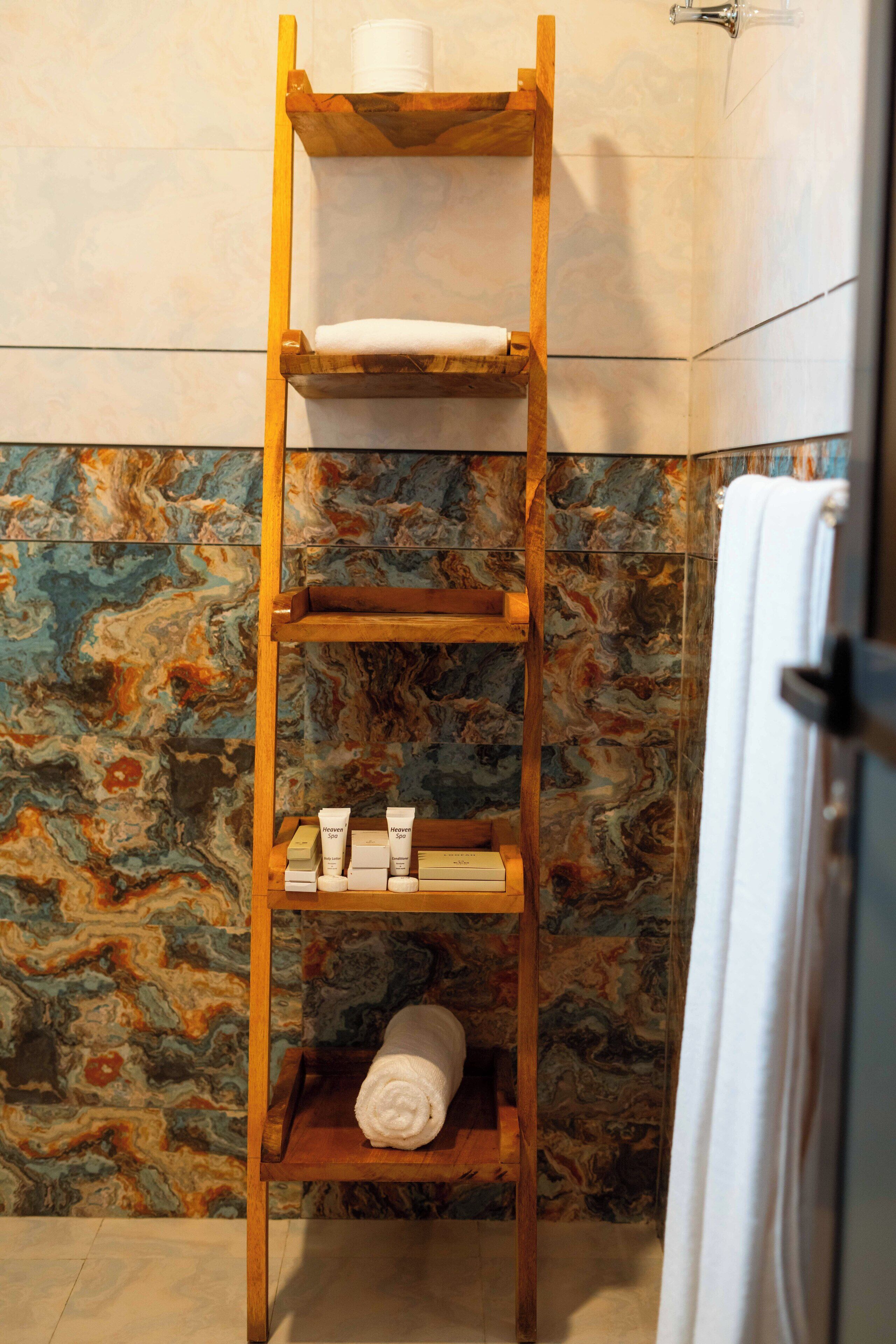 A wooden shelf with towels and toiletries in a bathroom with a marble backsplash.