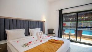 Ett hotellrum med en säng, ett nattduksbord, en stol, ett litet bord och utsikt över en swimmingpool.