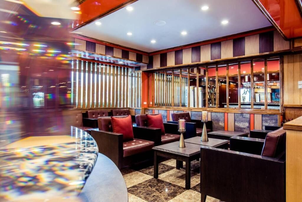 A modern hotel lobby with leather seating, a checkered floor, and a large window with vertical blinds.