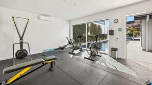 Et moderne fitnesscenter med træningsudstyr, en bænk og udsigt til en swimmingpool.