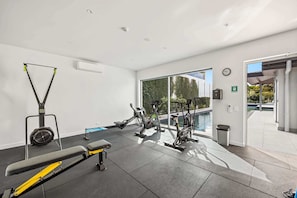 Un gimnasio moderno con equipo de ejercicio, una banca y vistas a una piscina.