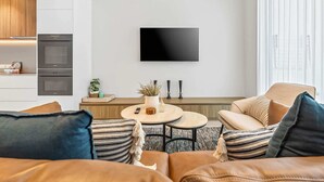 En moderne stue med en sofa, et sofabord og et fjernsyn monteret på væggen.