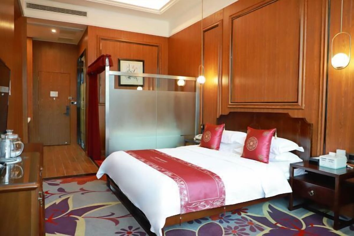 A hotel room with a bed, a nightstand, a wooden wardrobe, and a bathroom door.
