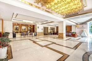 A hotel lobby with a reception desk, seating area, and a large decorative ceiling.