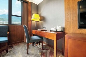 Une chambre d’hôtel avec un bureau en bois, une chaise, une lampe, un téléviseur et une vue sur un pont.