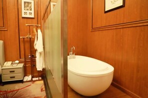 Une salle de bain avec une grande baignoire, un porte-serviettes, une petite table de chevet et un tableau encadré au mur.