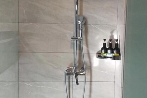 A shower with a handheld showerhead and a wall-mounted faucet. There are three bottles on a shelf to the right. - Chongqing Yuhao Hotel (Chongqing)