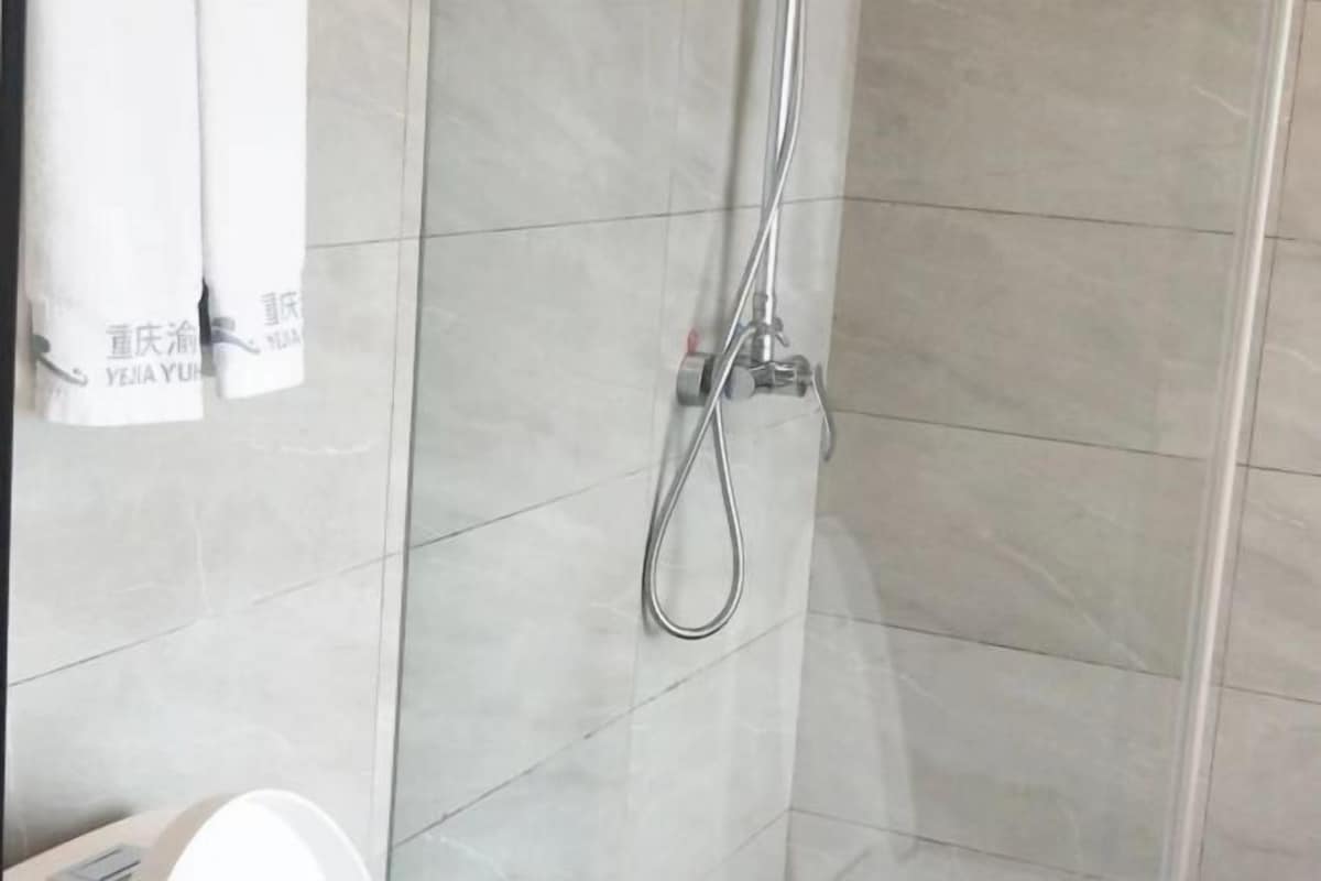 A shower with a handheld showerhead, tiled walls, and a towel hanging on a rack.