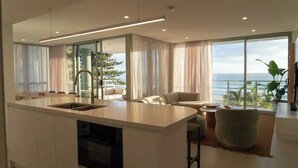 A modern kitchen with a central island, large windows with ocean views, and a cozy seating area with a view. - Apartment in Palm Beach (Palm Beach)