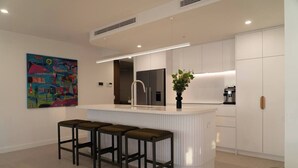 A modern kitchen with a central island, bar stools, a refrigerator, and a coffee machine. - Apartment in Palm Beach (Palm Beach)