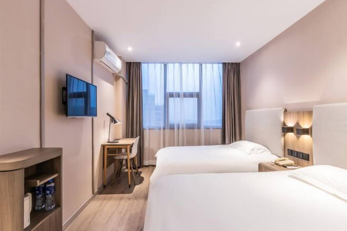 A hotel room with two beds, a desk, a TV, and a minibar.