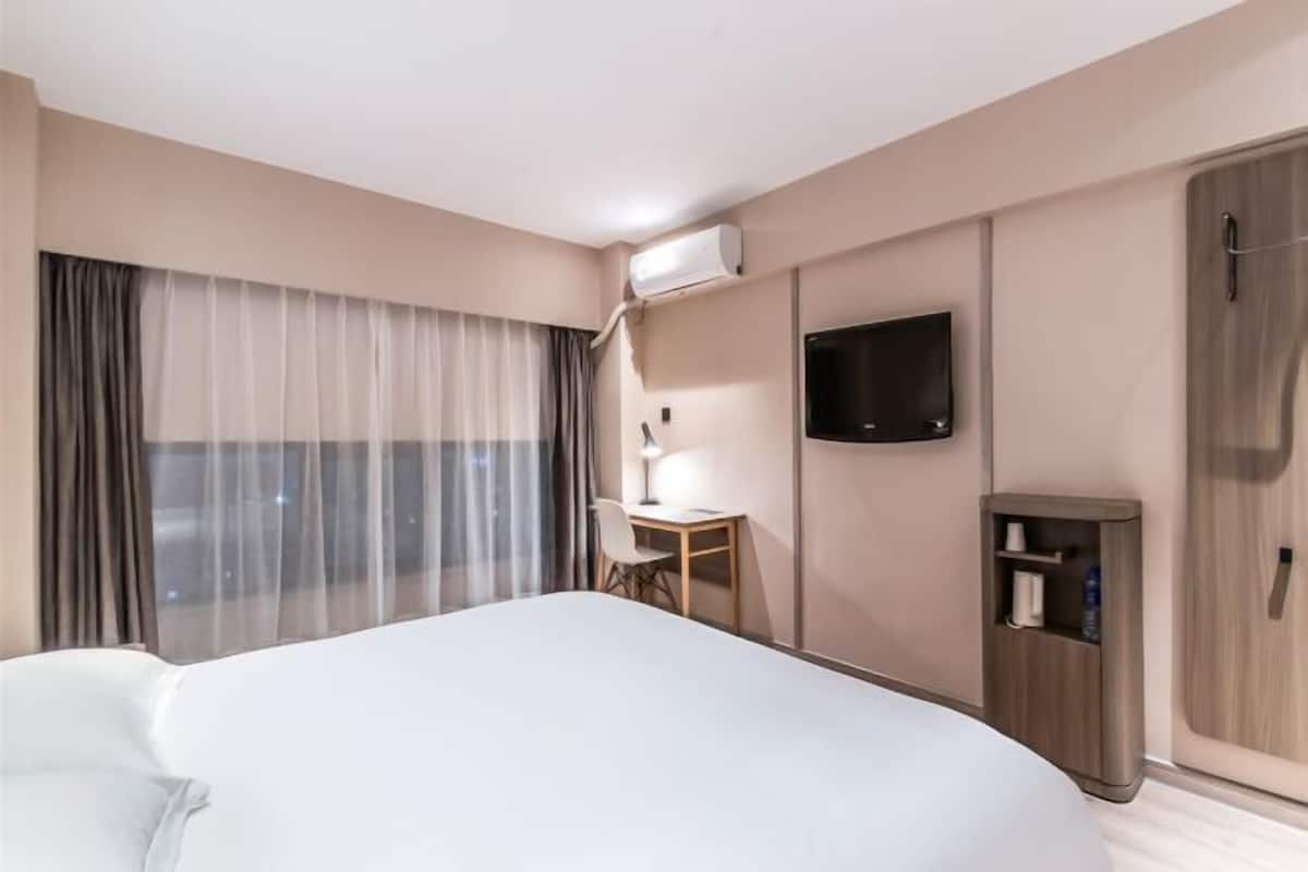 A hotel room with a bed, a desk, a TV, and a wardrobe.