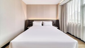 A modern hotel room with a large bed, a headboard with integrated lighting, a nightstand, and a view of the city through sheer curtains. - Hanting Hotel (Hangzhou)