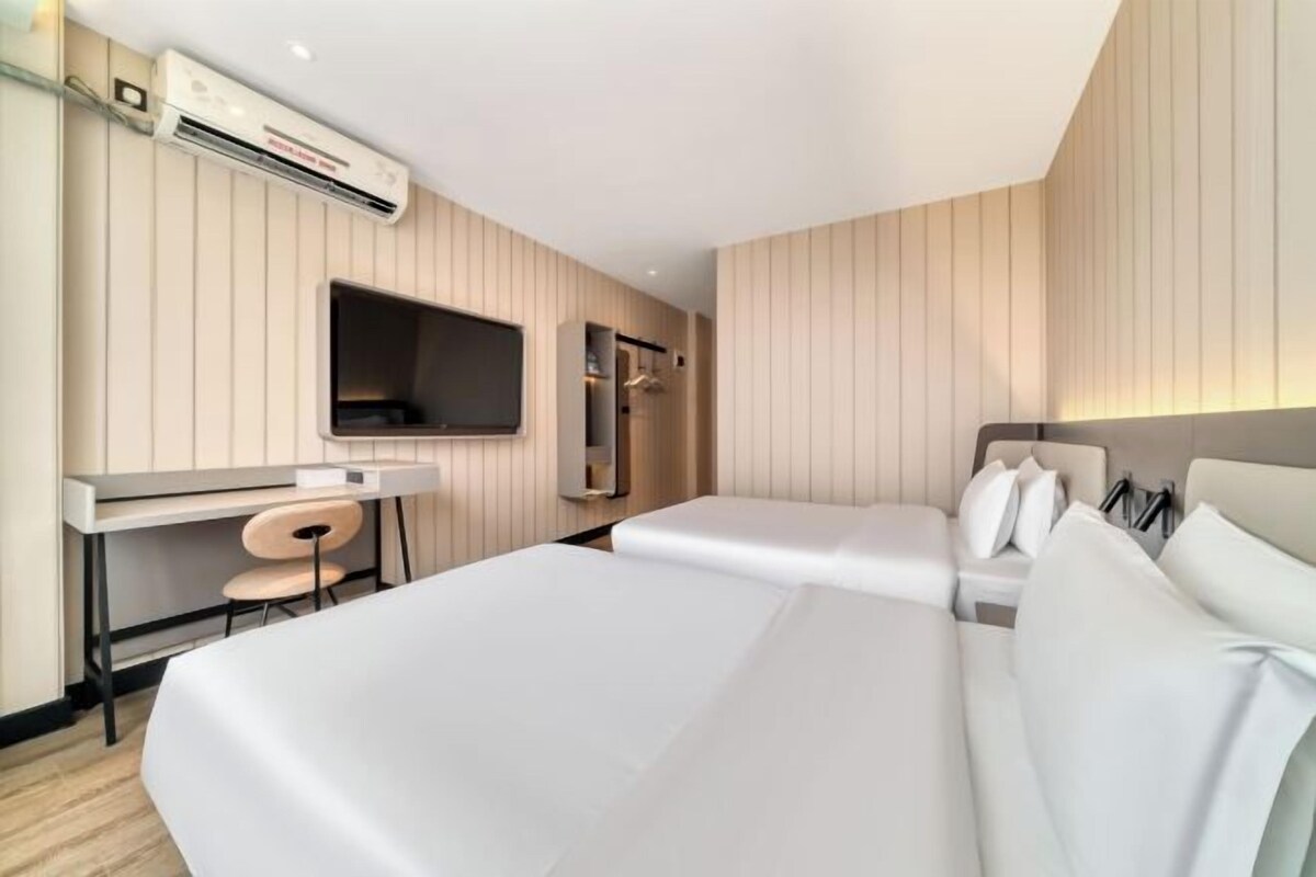 A hotel room with two beds, a desk, a chair, a TV, and a wardrobe.