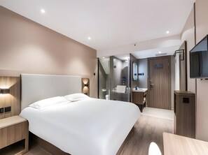 A modern hotel room with a large bed, bedside tables, a mirror, a TV, and a bathroom with a sink and mirror. - Hanting Hotel (Hangzhou)