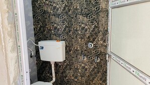 A bathroom with a toilet, a blue bucket, and a white toilet tank. - Hotel RajKamal (Shiv)