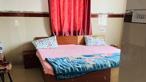 A bedroom with a bed, a ceiling fan, a red curtain, and a water bottle on a nightstand. - Hotel RajKamal (Shiv)