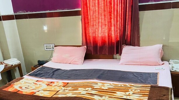 A hotel room with a bed, a nightstand, a power outlet, and a curtain. - Hotel RajKamal (Shiv)