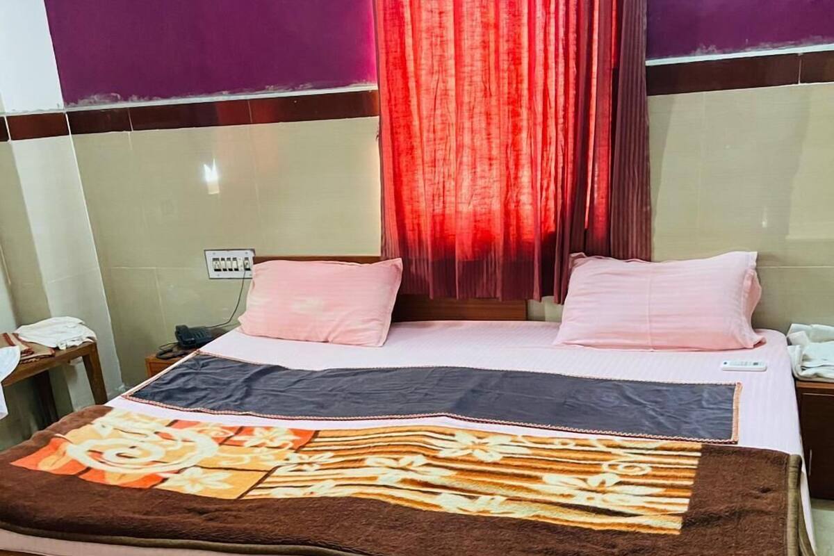 Une chambre d’hôtel avec un lit, une table de chevet, une prise de courant et un rideau.