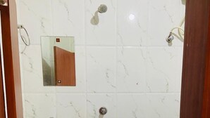 A bathroom with a sink, mirror, shower, and a bucket. - Hotel RajKamal (Shiv)