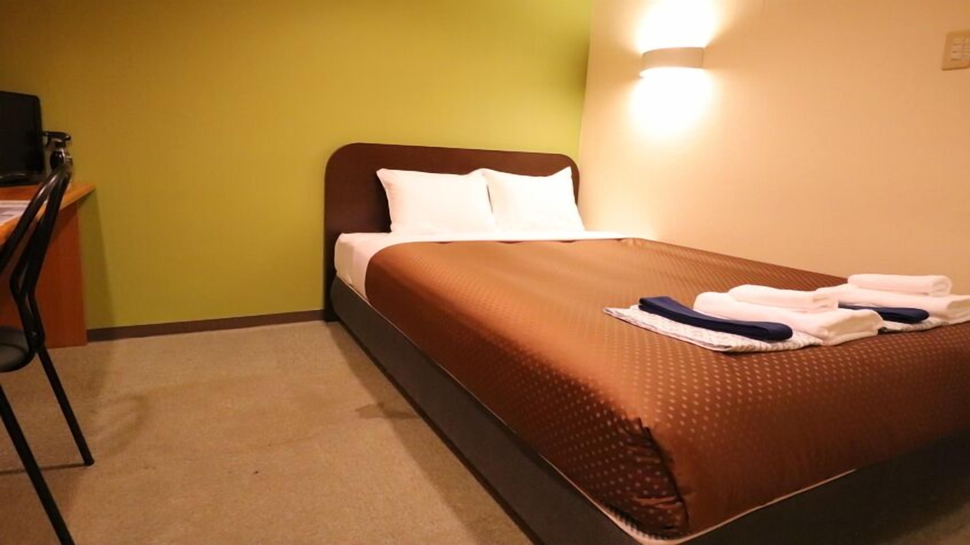 Een hotelkamer met een bed, kussens, een bureau en een stoel.