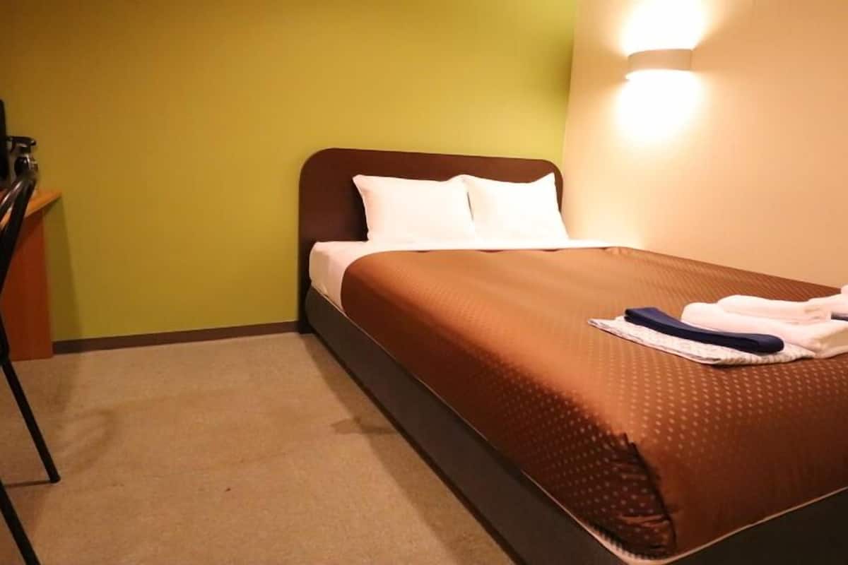 A hotel room with a bed, pillows, a desk, and a chair.