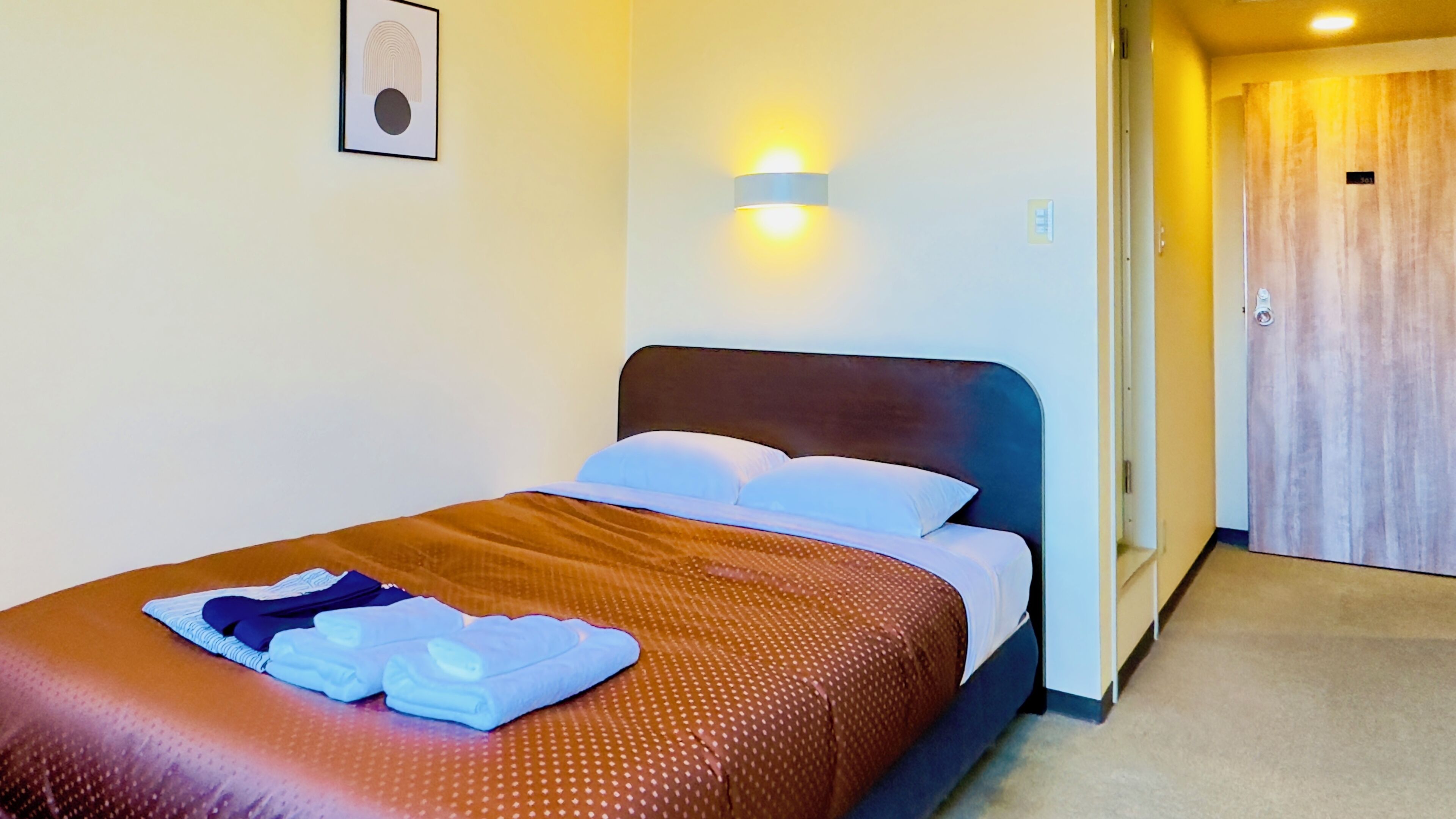 A hotel room with a bed, a wall-mounted light, and a door.
