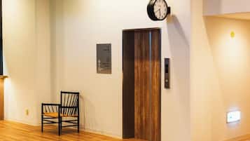 A hotel lobby with a wooden floor, a black chair, a clock, and a door with a sign indicating the restroom and guest elevator.
