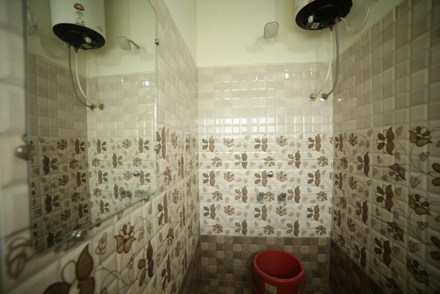 Un baño con baldosas estampadas, zona de ducha y un cubo rojo.