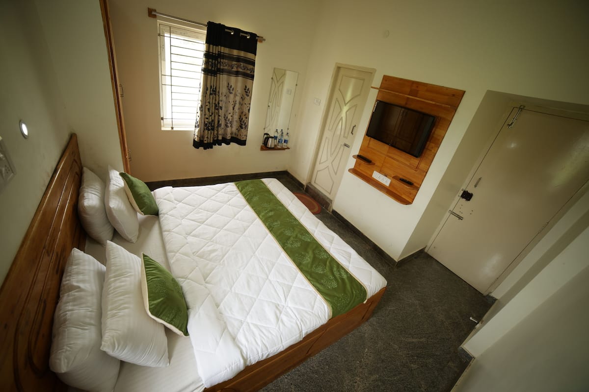 Ein Schlafzimmer mit Bett, Vorhängen an einem Fenster, einem Fernseher und einer Tür.