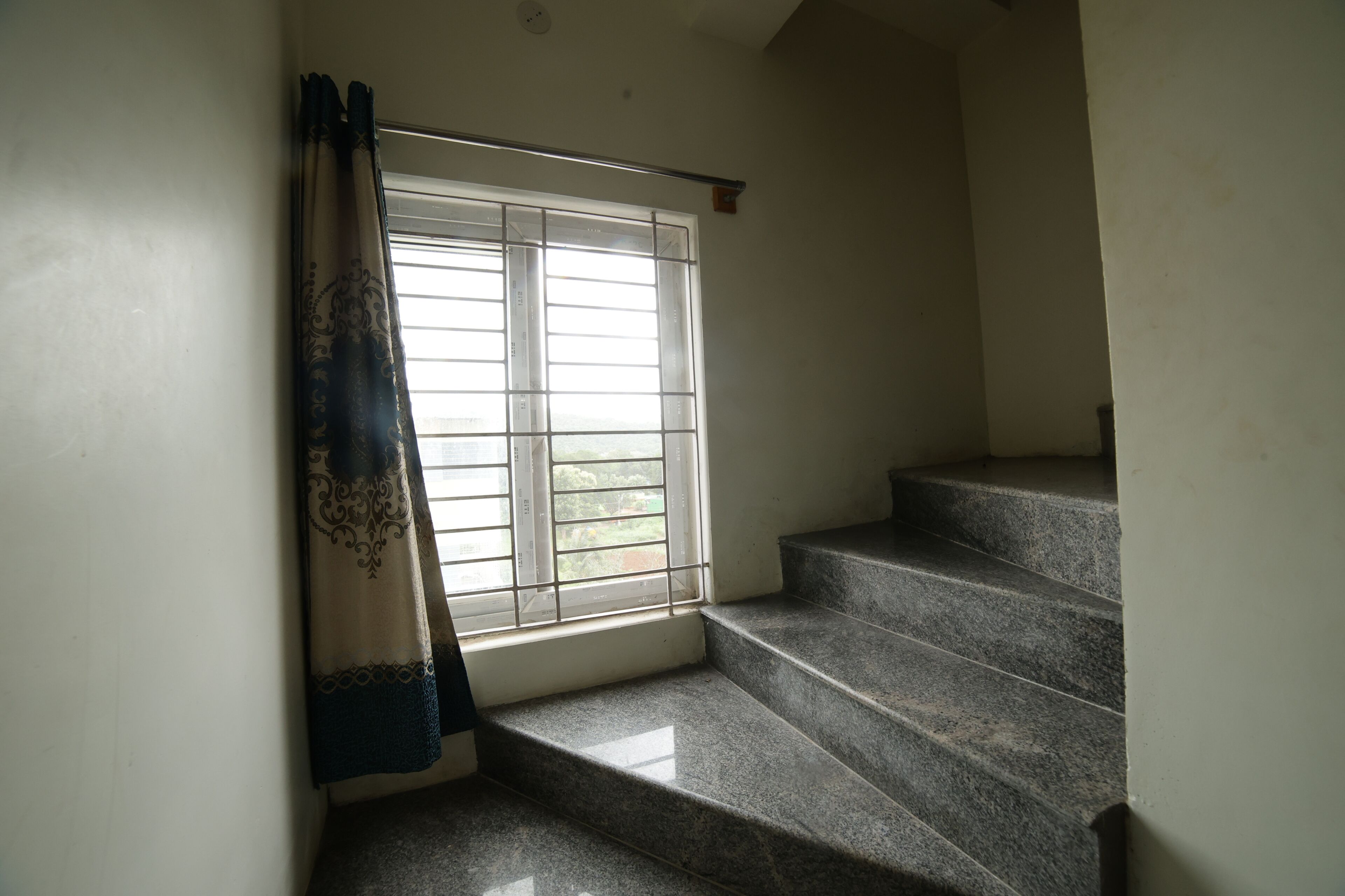 A staircase leading to a landing with a window and a curtain.