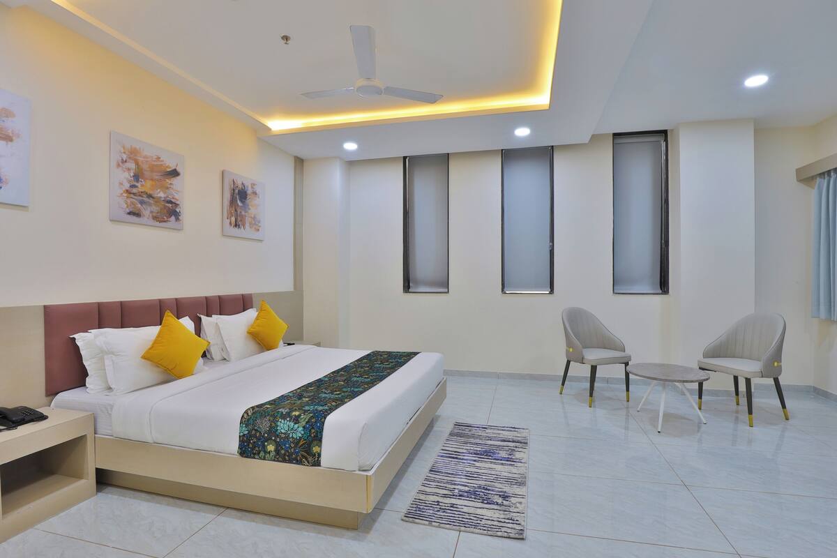 Una habitación de hotel moderna con cama, mesita de noche, dos sillas, ventilador de techo y obras de arte en las paredes.