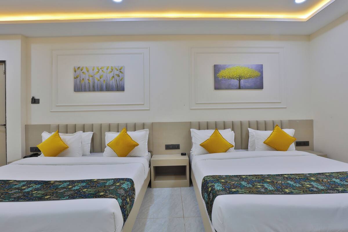 Habitación de hotel con dos camas, cada una con ropa blanca y almohadas amarillas. Dos mesitas de noche están situadas entre las camas, y hay obras de arte colgadas sobre cada cama.