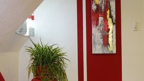 A room with a red sofa, a potted plant, and a wall with abstract art. - Apartment 'Wassergartenparadies' with Shared Terrace, Shared Garden and Wi-Fi (Harsdorf)