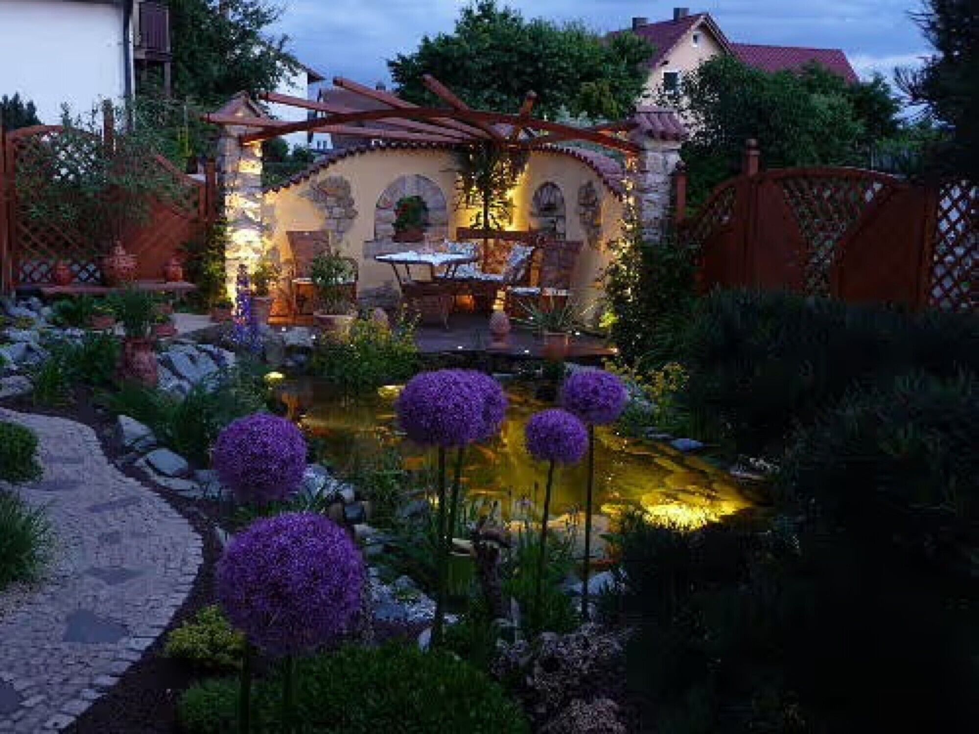 Un jardín con un estanque, un pérgola y una zona de comedor.