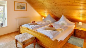 Un dormitorio con techo de madera, dos camas, una ventana, un radiador y un cuadro enmarcado en la pared.
