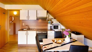 Cocina compacta con gabinetes blancos, un fregadero, estufa y microondas. Hay una zona de comedor con una mesa y sillas, y un florero con flores sobre la mesa.