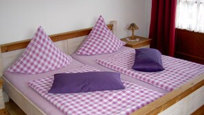 Un lit avec une couvre-lit à carreaux et des oreillers, une tête de lit en bois, une table de chevet avec une lampe et une fenêtre avec des rideaux rouges.