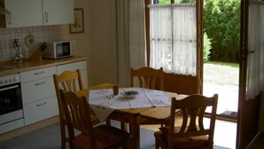 Une cuisine équipée d’une table à manger, de chaises, d’un four à micro-ondes et offrant une vue sur un jardin grâce à une porte vitrée.