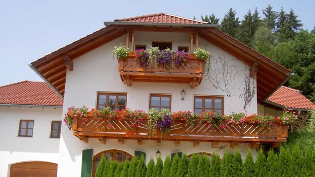 Une maison à deux étages avec un balcon, une porte en bois et une haie bien entretenue.