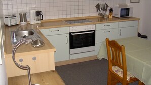 Une cuisine compacte équipée d’un évier, d’une cuisinière, d’un four à micro-ondes et d’un coin repas avec une table et une chaise.
