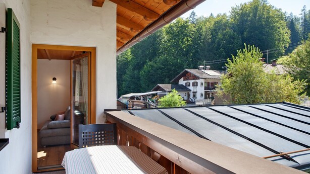 A balcony with a table and chairs, a wooden ceiling, and a view of a village and forest. - Apartment 'Ferienwohnung Waxensteinblick' with Mountain View, Balcony and Wi-Fi (Grainau)