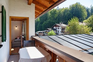 Un balcón con mesa y sillas, techo de madera y vistas a un pueblo y bosque.
